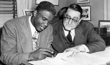 Jackie Robinson signing his initial contract with the Brooklyn Dodgers, alongside general manager Branch Rickey. 